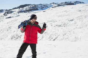 Skier carrying skis over shoulder on flat snowfield at foot of snowy ridge, checking device