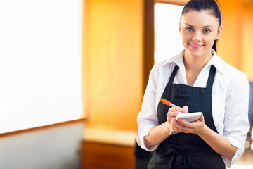 Woman holding pen over order pad while wearing black apron taking order in restaurant, copy space