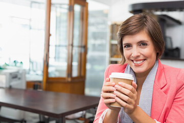Woman in thirties wearing coral blazer and scarf holding paper coffee cup at office, copy space