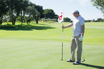 Man standing on golf course putting green holding flagstick and putter while gazing across fairway
