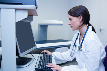 Medical imaging equipment standing by desktop monitor and keyboard in light-colored clinical room
