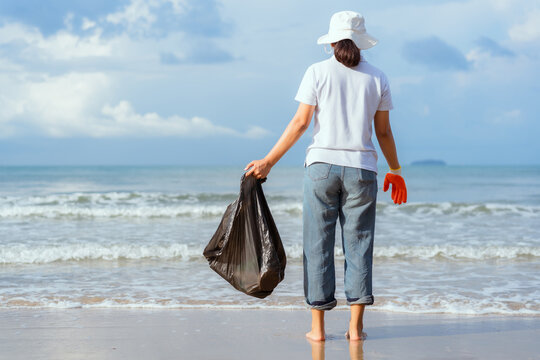 Person collecting trash on a beach during a sunny day by the ocean with palm trees in the background