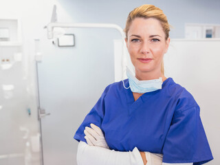 Female clinician standing in clinic wearing scrubs, mask and gloves with exam light, copy space