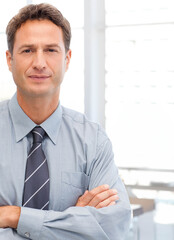 Mid adult man standing wearing blue shirt, striped tie by window blinds in office, copy space
