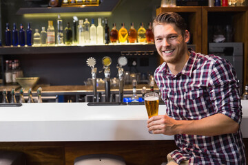 Man sitting at bar counter holding tall beer glass with metal taps, illuminated bottles, copy space