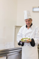 Male chef holding plate of fresh salad toward camera in professional kitchen, copy space