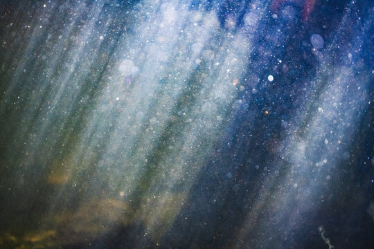 Sunlight streaming through blue and green water with abstract bubbles all around. Rocks and riverbed can be faintly seen at the bottom