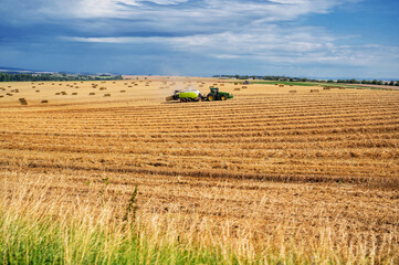 Tractor with straw baler on field during harvest. Agriculture work.