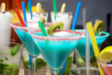 Colorful tropical cocktails in martini glasses closeup. Blue drink with sugar rim and kiwi garnish. Refreshing summer beverages with lemon, mint and straws. Perfect exotic party drinks for warm sunny.