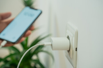 Close-up of a smartphone connected to a wall socket with a USB cable for charging. Modern technology and home electricity concept.