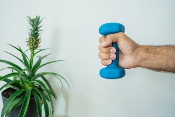Close-up of a man lifting a small blue dumbbell for strength training at home. Healthy lifestyle and fitness concept with focus on arm muscles.
