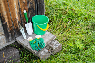 Green garden bucket, shovel, pruning shears and gloves on wooden planks.