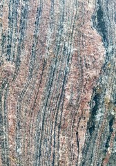 Closeup of the texture of raw granite with stripes of pink, greay and black.  Background