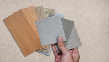 interior architect compares quartz stone samples with wooden laminated chart showing different types of wood, different colors and textures  textures on beige marble background.