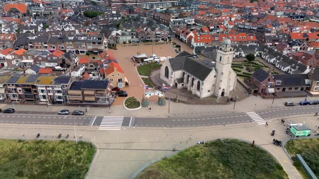 Katwijk aan Zee, South Holland, Netherlands - 09.06.2025: Aerial view of a coastal European town with red-roofed houses, a central church, and a geometric garden. A wide road with cars