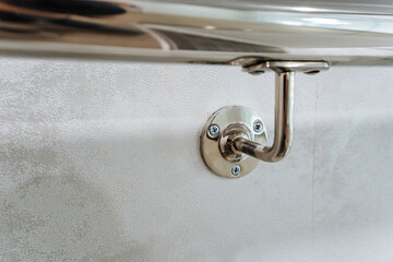 The image shows a closeup of a polished chrome shower curtain rod bracket, securely mounted on a...