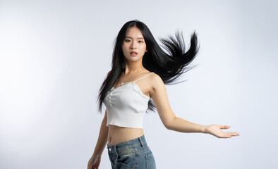 Beautiful woman tossing her black hair while wearing a white crop top and blue jeans