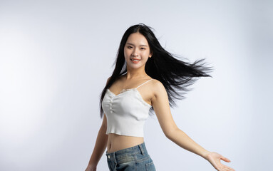 Smiling woman with flowing black hair in a studio setting wearing a white top and jeans