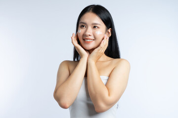 A woman with dark hair smiles applying cream to her face while resting her face in her hands