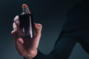 female hand with bottle of perfume on dark background