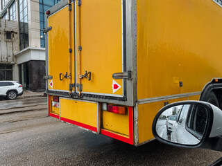 This closeup shows a vibrant yellow delivery truck with bright reflective markings in a bustling...