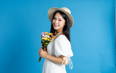 Smiling woman in a white dress and hat holding a bouquet against a vibrant blue background