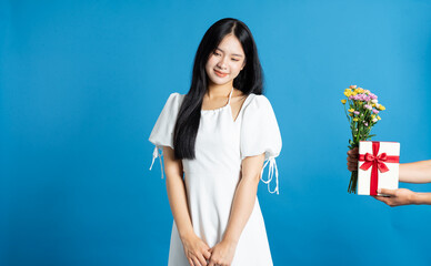An elegant young lady receives a thoughtful gift of flowers and a present on a blue backdrop