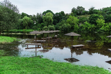Wooden parasols poke out of the river, partially flooded and casting mirrored reflections on the...