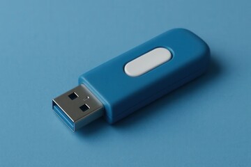 A solitary blue USB flash drive rests on a textured blue surface, its white button standing out against the cool hue