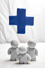 Three clay figures gathered beneath a large blue medical cross, representing access to healthcare...