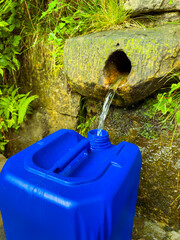 The scene showcases refreshing spring water flowing gently into a blue container, beautifully...