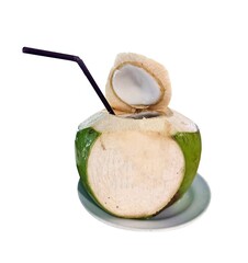 A close-up, high-angle shot captures a freshly opened young green coconut with a black straw inserted, placed on a simple white plate. The focus is sharp on the coconut's opened top and the clear
