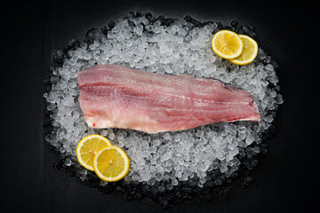 Fresh fish fillet on ice on a dark background with lemons