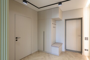 bright and minimalist hallway with neutral tones, featuring built-in storage, a bench, and modern lighting. The herringbone floor adds texture