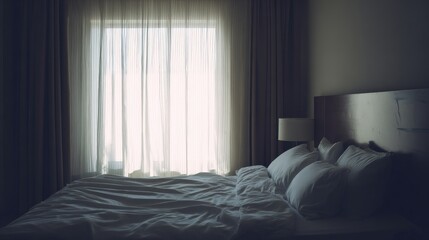 An unmade bed in a dimly lit room with rumpled sheets, stacked pillows, and sheer curtains allowing diffused light,