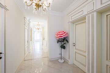 Elegant hallway with marble floor, white walls, and ornate doors. A large pink rose sculpture...