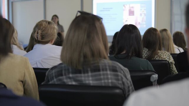 Group of people are sitting in a classroom. A woman is standing in front of a projector screen