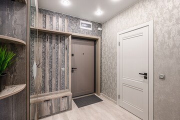 Cozy entryway with wood-paneled storage, textured wallpaper, and a beige front door. White interior...