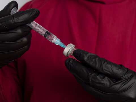 Close-up of a doctor, nurse, or scientist filling or drawing a syringe with medication from a vial. A doctor wearing a red surgical gown drawing fluid from a vial with copy space. Medical concept.