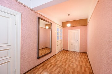 Hallway with pink wallpaper, wood floors, and white doors. A large mirror reflects the space, enhancing the room's depth
