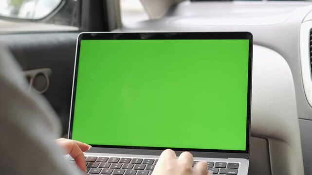 Person is typing on a laptop with a green screen. The laptop is open and the person is using the keyboard