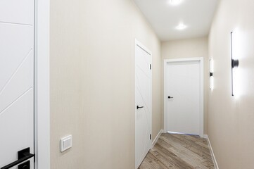 Bright hallway with modern white doors, wood flooring, and sleek wall-mounted lights. Minimalist interior design