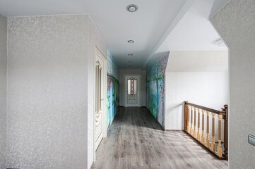 Bright hallway with patterned walls, wooden floors, and doors. One wall features scenic artwork. Stair railing visible