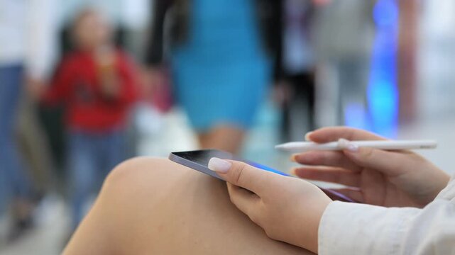 Woman is sitting on a couch with a cell phone in her hand. She is also holding a pen