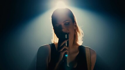 Woman singing on stage with vintage microphone and spotlight during emotional live music performance in dark moody setting with dramatic lighting and expressive facial expression