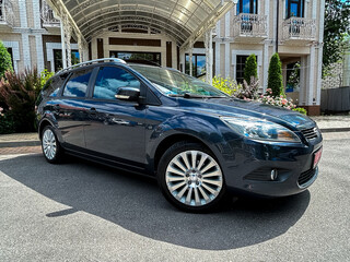 A stylish blue hatchback is elegantly parked right in front of a luxurious and grand building,...