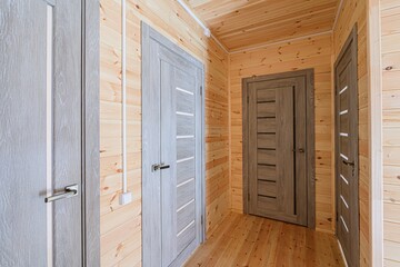 rustic hallway features wood paneling, flooring, and gray modern doors, creating a warm, cabin-like...