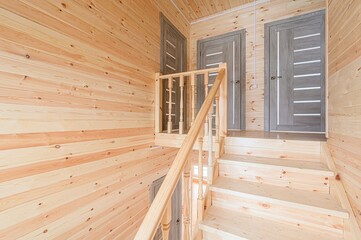 Interior shot of wooden staircase leading to two gray doors. The walls and stairs are wood-paneled....