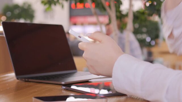 Person is sitting at a table with a laptop and two cell phones. They are using one of the cell phones to text