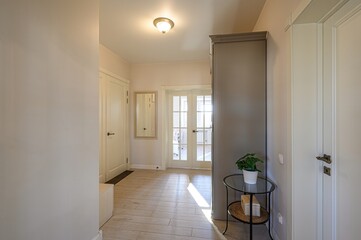 hallway with neutral walls, light wood floors, and white doors. A gray cabinet stands near a...
